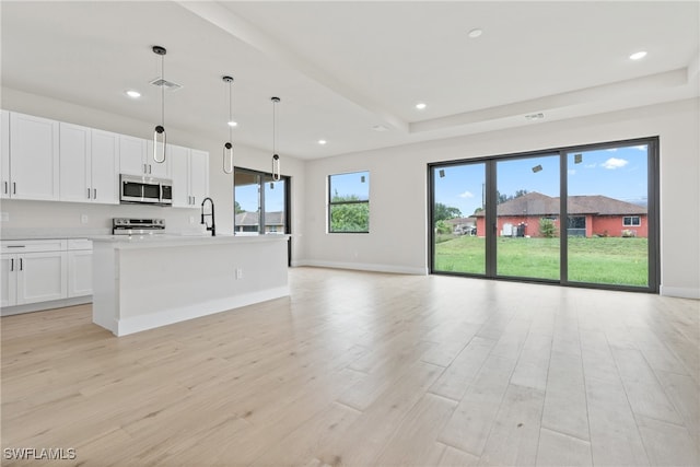 kitchen featuring white cabinets, a kitchen island with sink, light wood-type flooring, pendant lighting, and stainless steel appliances