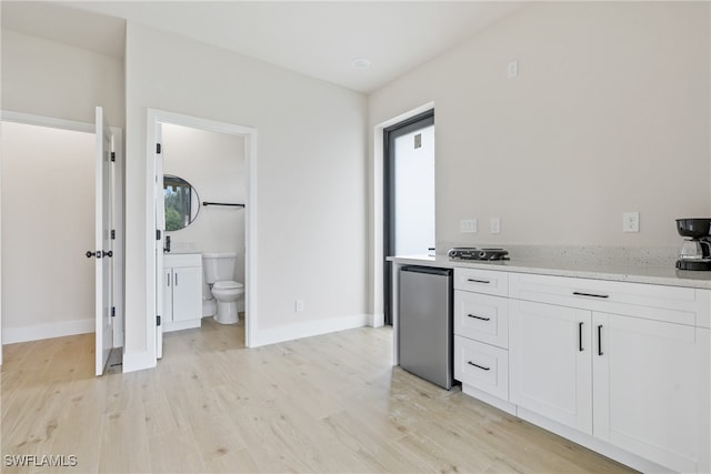 kitchen with light hardwood / wood-style floors, white cabinetry, light stone countertops, and stainless steel refrigerator