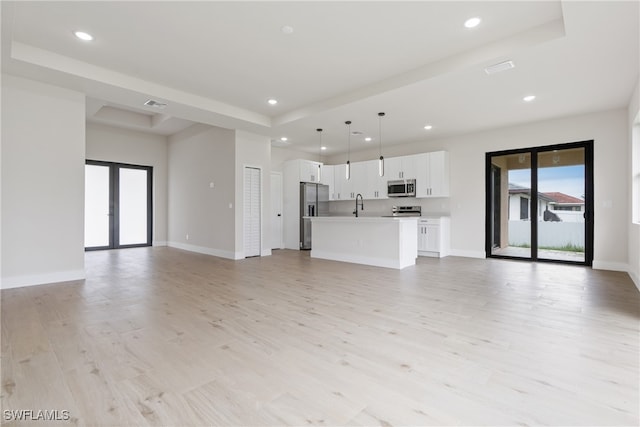 unfurnished living room featuring sink, french doors, a tray ceiling, and light wood-type flooring