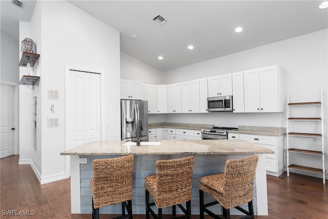 kitchen with a breakfast bar, dark hardwood / wood-style floors, stainless steel appliances, and a center island with sink