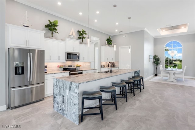 kitchen with a center island with sink, decorative backsplash, light stone countertops, appliances with stainless steel finishes, and white cabinetry