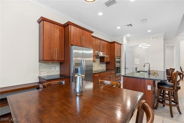 kitchen featuring stainless steel appliances, backsplash, ornamental molding, and a kitchen island with sink