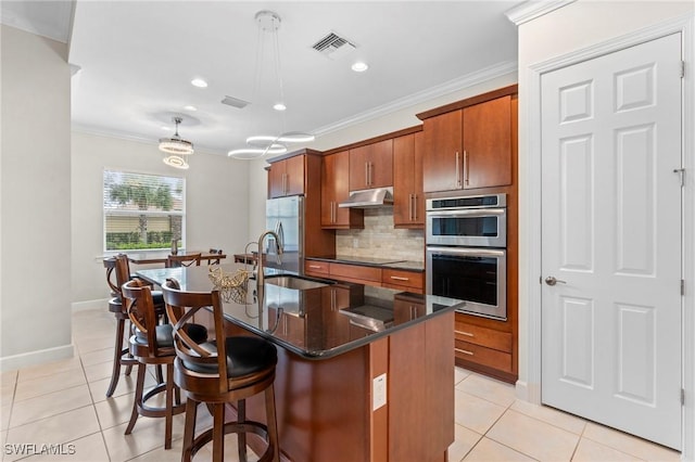 kitchen featuring backsplash, appliances with stainless steel finishes, an island with sink, pendant lighting, and light tile patterned flooring