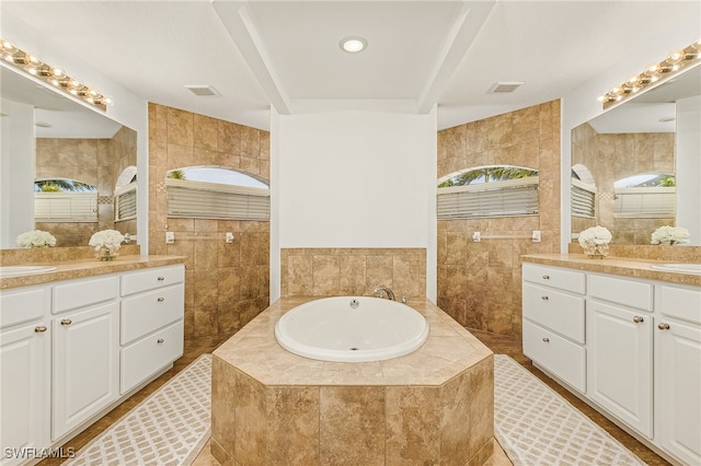 bathroom with vanity, a relaxing tiled tub, and tile walls