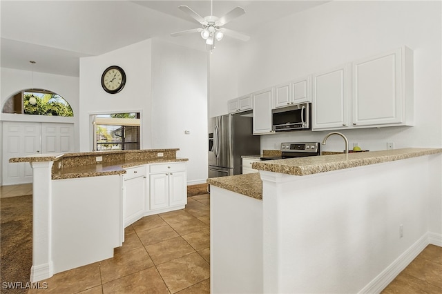 kitchen featuring kitchen peninsula, a breakfast bar, white cabinets, appliances with stainless steel finishes, and a towering ceiling