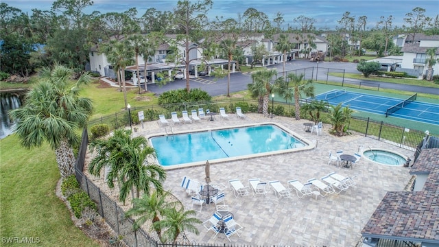 pool with a hot tub, a lawn, a tennis court, a residential view, and fence