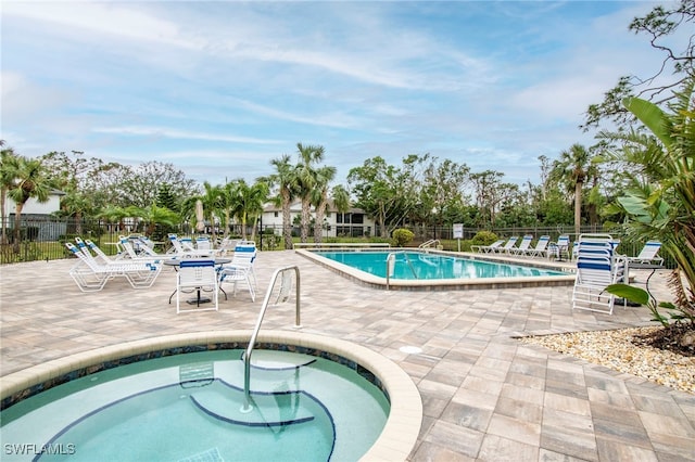 community pool with fence, a hot tub, and a patio