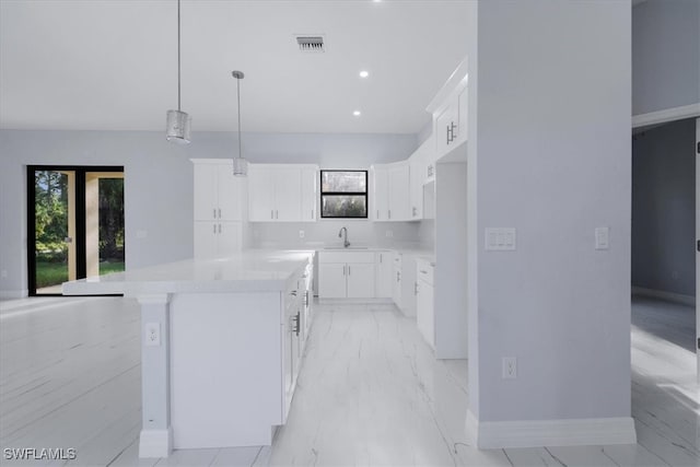 kitchen featuring light stone countertops, sink, a kitchen island, hanging light fixtures, and white cabinets