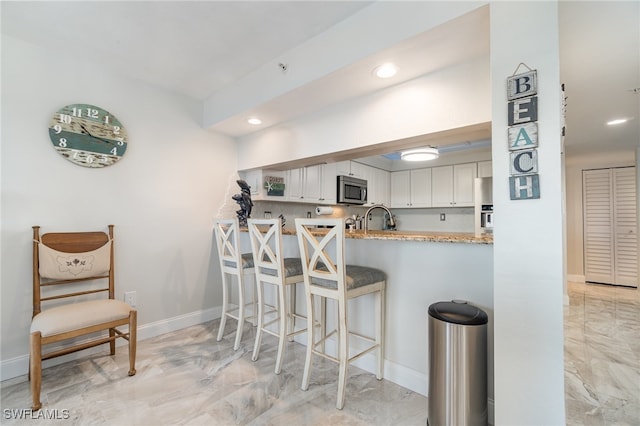 kitchen featuring stainless steel appliances, white cabinetry, sink, a breakfast bar area, and kitchen peninsula