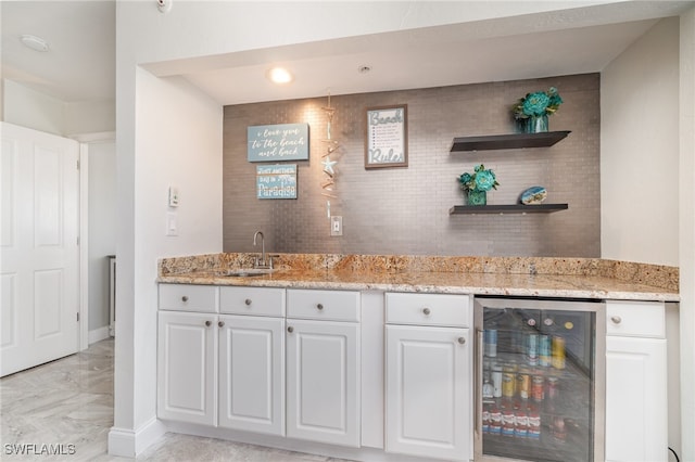 kitchen with white cabinetry, light stone countertops, sink, and wine cooler