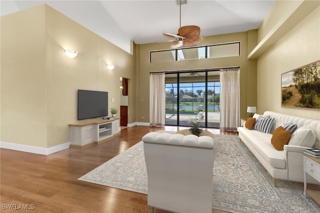 living room with ceiling fan, a high ceiling, and wood-type flooring