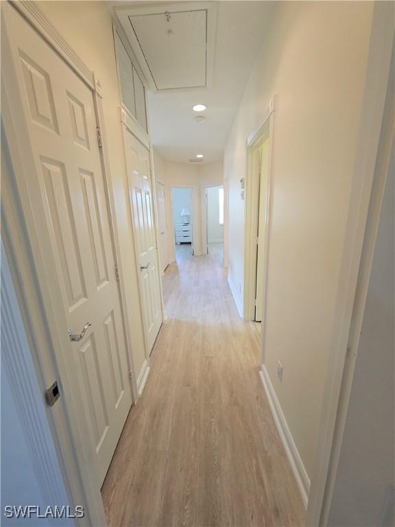 hallway featuring light wood-type flooring, attic access, and baseboards