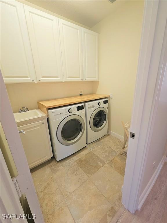 clothes washing area with baseboards, a sink, cabinet space, and washing machine and dryer