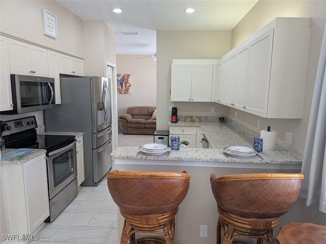 kitchen with light stone countertops, white cabinets, a kitchen bar, stainless steel appliances, and kitchen peninsula