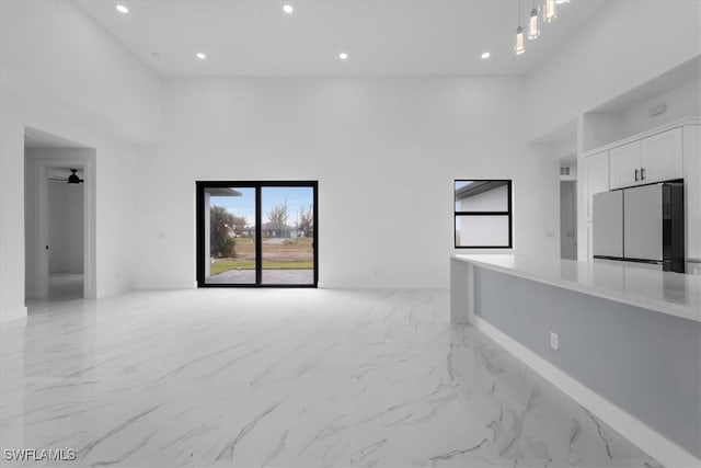 unfurnished living room featuring ceiling fan and a high ceiling