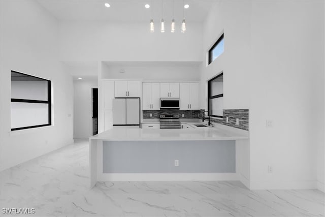 kitchen featuring a high ceiling, hanging light fixtures, stainless steel range with electric stovetop, white cabinets, and white fridge