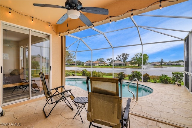 view of pool with glass enclosure, a patio area, a water view, and ceiling fan