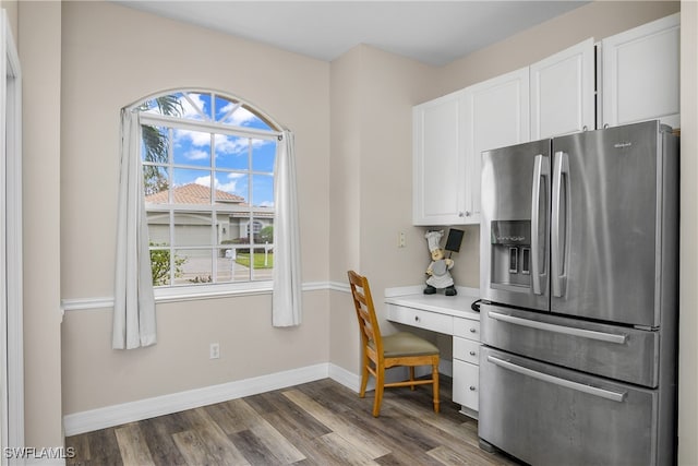 kitchen with dark wood-type flooring, stainless steel fridge with ice dispenser, built in desk, and white cabinets