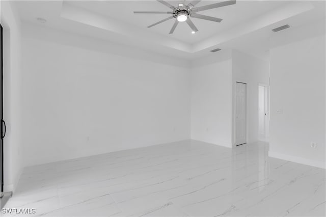 empty room with ceiling fan and a raised ceiling