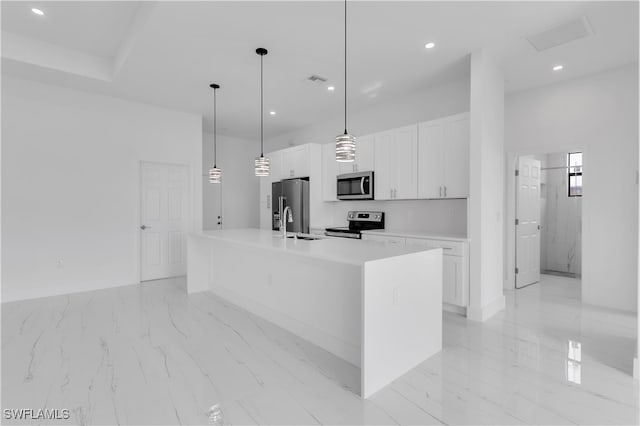 kitchen with appliances with stainless steel finishes, sink, white cabinetry, decorative light fixtures, and a center island with sink