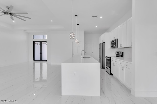 kitchen featuring an island with sink, sink, white cabinets, decorative light fixtures, and appliances with stainless steel finishes