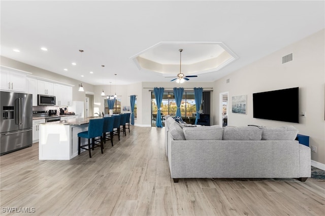 living room featuring a raised ceiling, ceiling fan, and light wood-type flooring