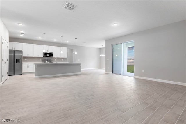 kitchen with a kitchen island with sink, white cabinets, pendant lighting, light wood-type flooring, and appliances with stainless steel finishes