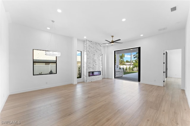 unfurnished living room featuring a premium fireplace, ceiling fan, and light wood-type flooring