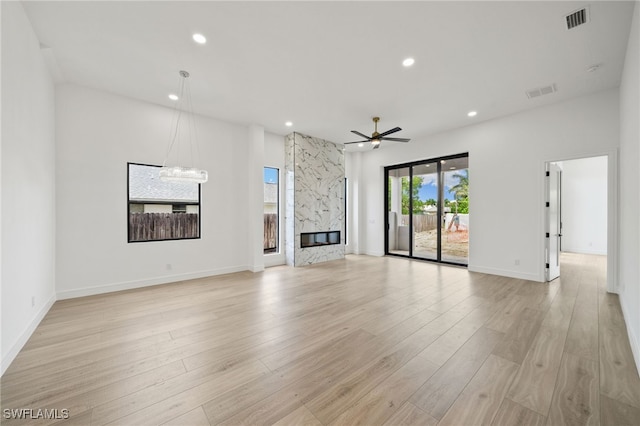 unfurnished living room featuring ceiling fan with notable chandelier, light wood-type flooring, and a high end fireplace