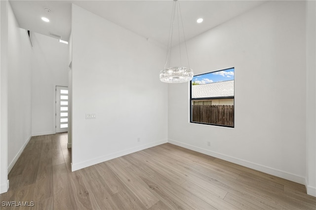 empty room with a high ceiling, light hardwood / wood-style flooring, and a notable chandelier