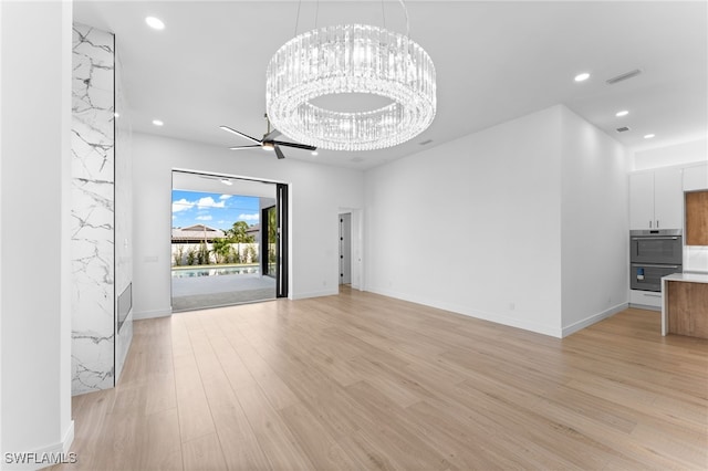 unfurnished living room featuring ceiling fan with notable chandelier and light hardwood / wood-style floors