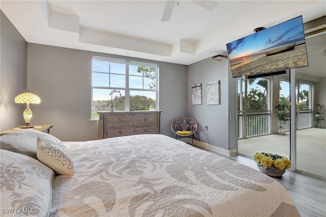 bedroom with light hardwood / wood-style flooring, a tray ceiling, access to outside, and ceiling fan