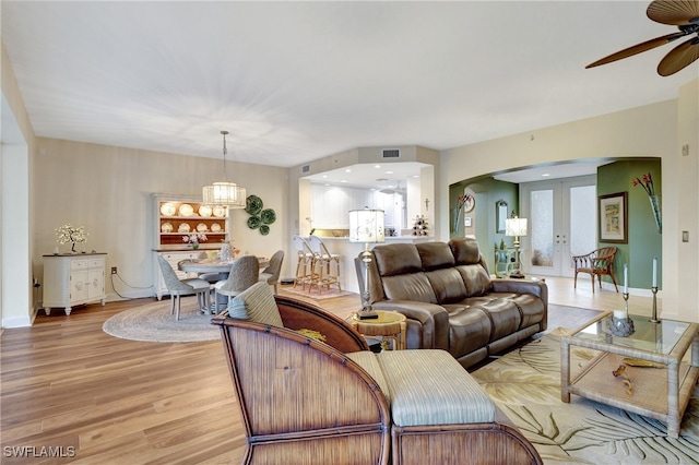 living room with french doors, ceiling fan with notable chandelier, and light hardwood / wood-style floors