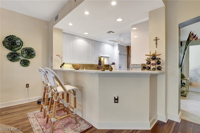 kitchen with decorative backsplash, white cabinetry, kitchen peninsula, and wood-type flooring