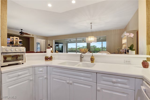 kitchen featuring kitchen peninsula, sink, decorative light fixtures, white cabinetry, and ceiling fan with notable chandelier