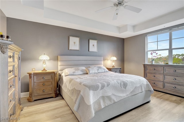 bedroom featuring light hardwood / wood-style flooring, a tray ceiling, and ceiling fan