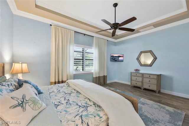 bedroom with baseboards, ornamental molding, a raised ceiling, and wood finished floors