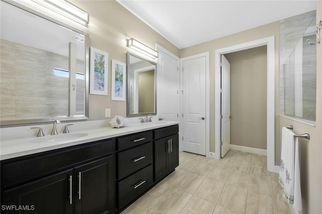 bathroom featuring a tile shower, double vanity, a sink, and baseboards