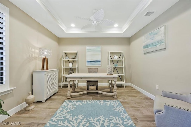 living area with light wood finished floors, baseboards, a tray ceiling, and crown molding