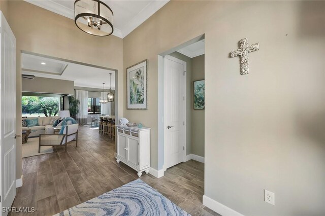 hallway featuring ornamental molding, dark wood-style flooring, a notable chandelier, and baseboards