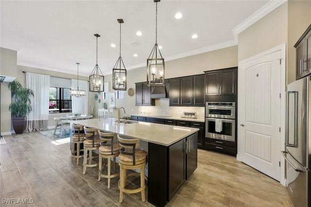 kitchen featuring a center island with sink, stainless steel appliances, light countertops, backsplash, and a sink