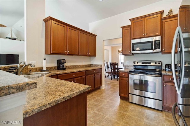 kitchen with lofted ceiling, kitchen peninsula, sink, light stone countertops, and appliances with stainless steel finishes