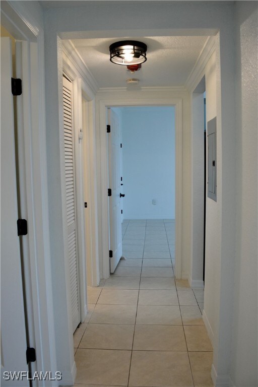 hall with ornamental molding, electric panel, and light tile patterned floors