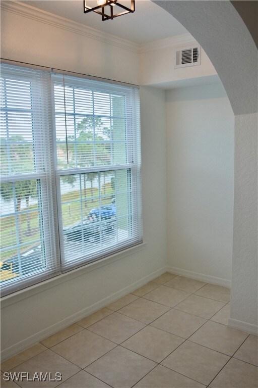 tiled spare room with ornamental molding and a chandelier