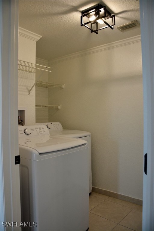 laundry room featuring washer / dryer, a textured ceiling, ornamental molding, and light tile patterned floors