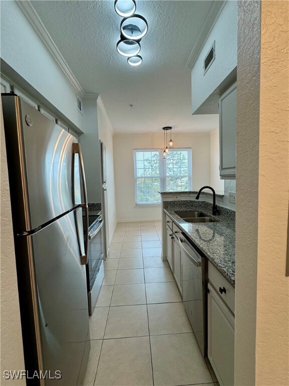 kitchen featuring appliances with stainless steel finishes, sink, dark stone countertops, crown molding, and light tile patterned floors