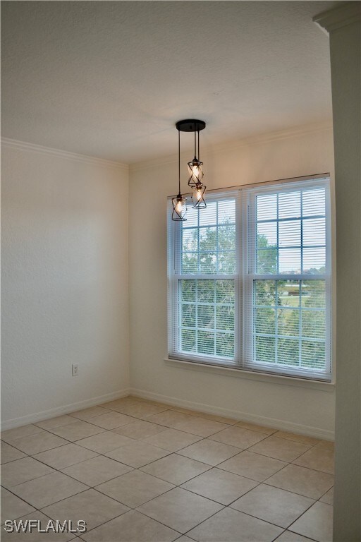 tiled empty room with a notable chandelier and ornamental molding