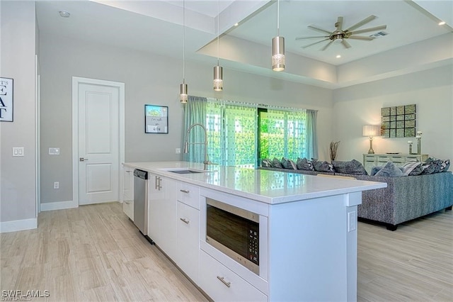 kitchen featuring a kitchen island with sink, hanging light fixtures, stainless steel appliances, sink, and white cabinets