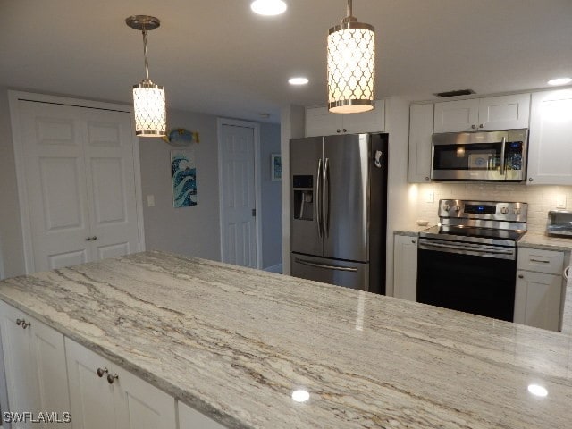 kitchen featuring light stone countertops, appliances with stainless steel finishes, decorative light fixtures, and white cabinets