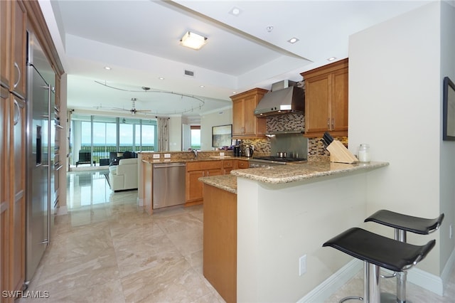 kitchen with kitchen peninsula, stainless steel appliances, a kitchen breakfast bar, and wall chimney range hood